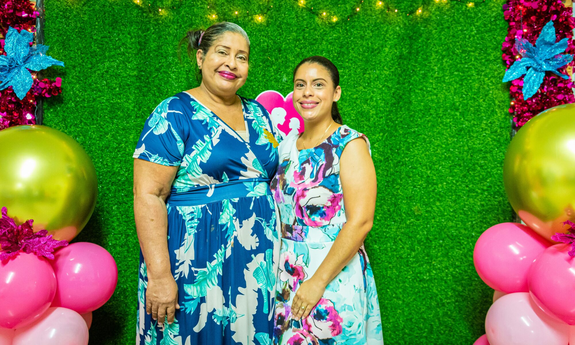 Two friends smiling and posing together in a photo booth, wearing fun props and making memories